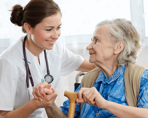 A happy elderly woman sitting down and holding hand with a caring young nurse.