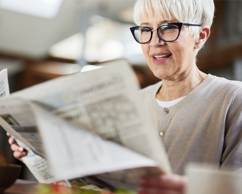 A happy elderly womman reading a newspaper