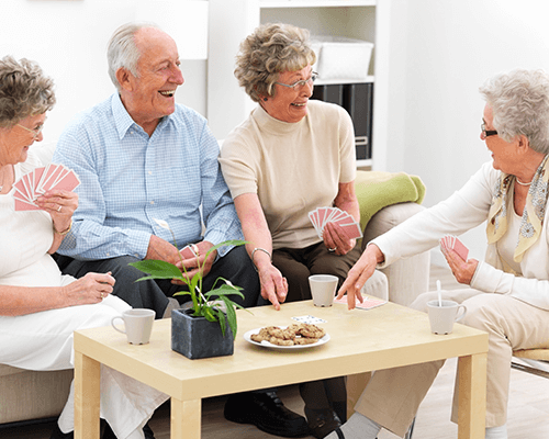 Four seniors enjoying a game of card and cookies with tea among friends.